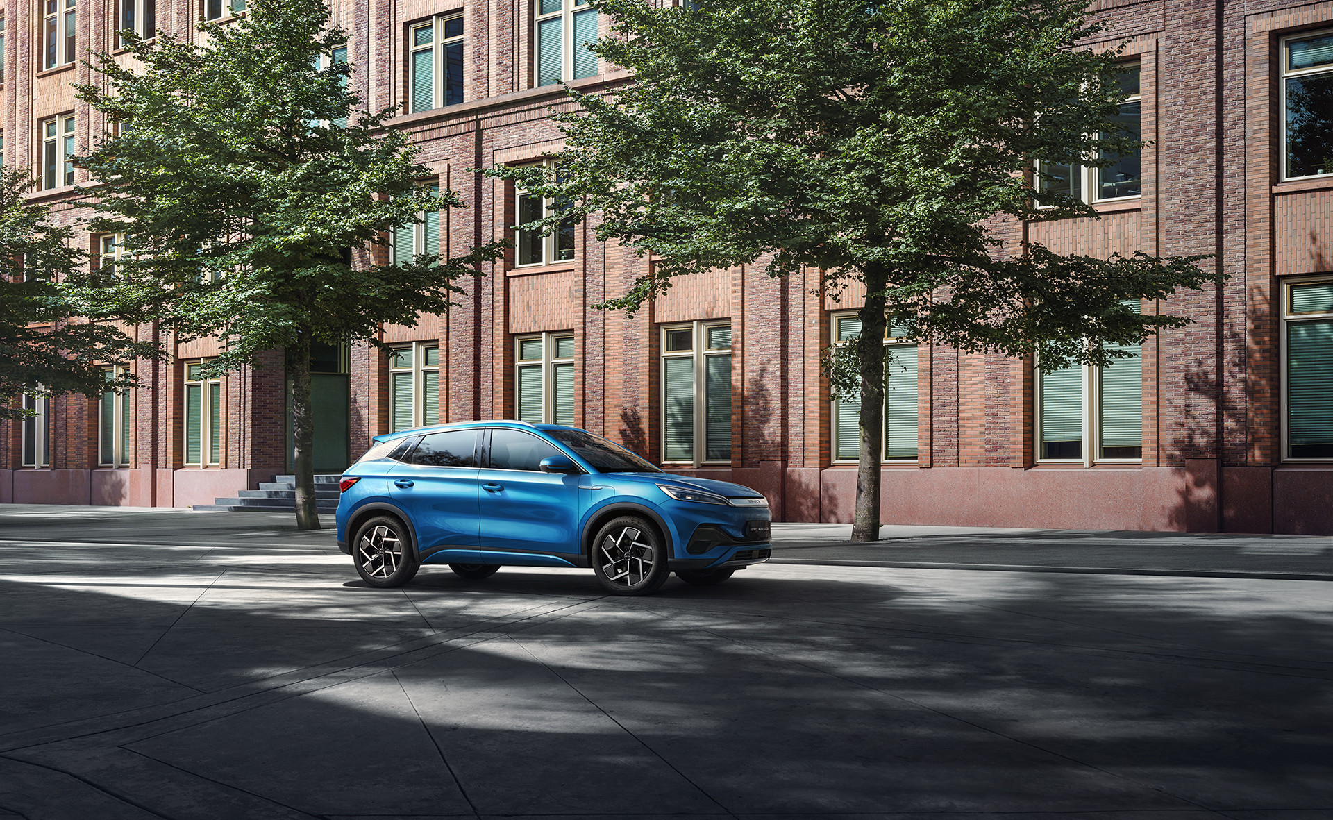 A photograph of a Surfing Blue BYD Atto 3 parked outside a building on a quiet street
